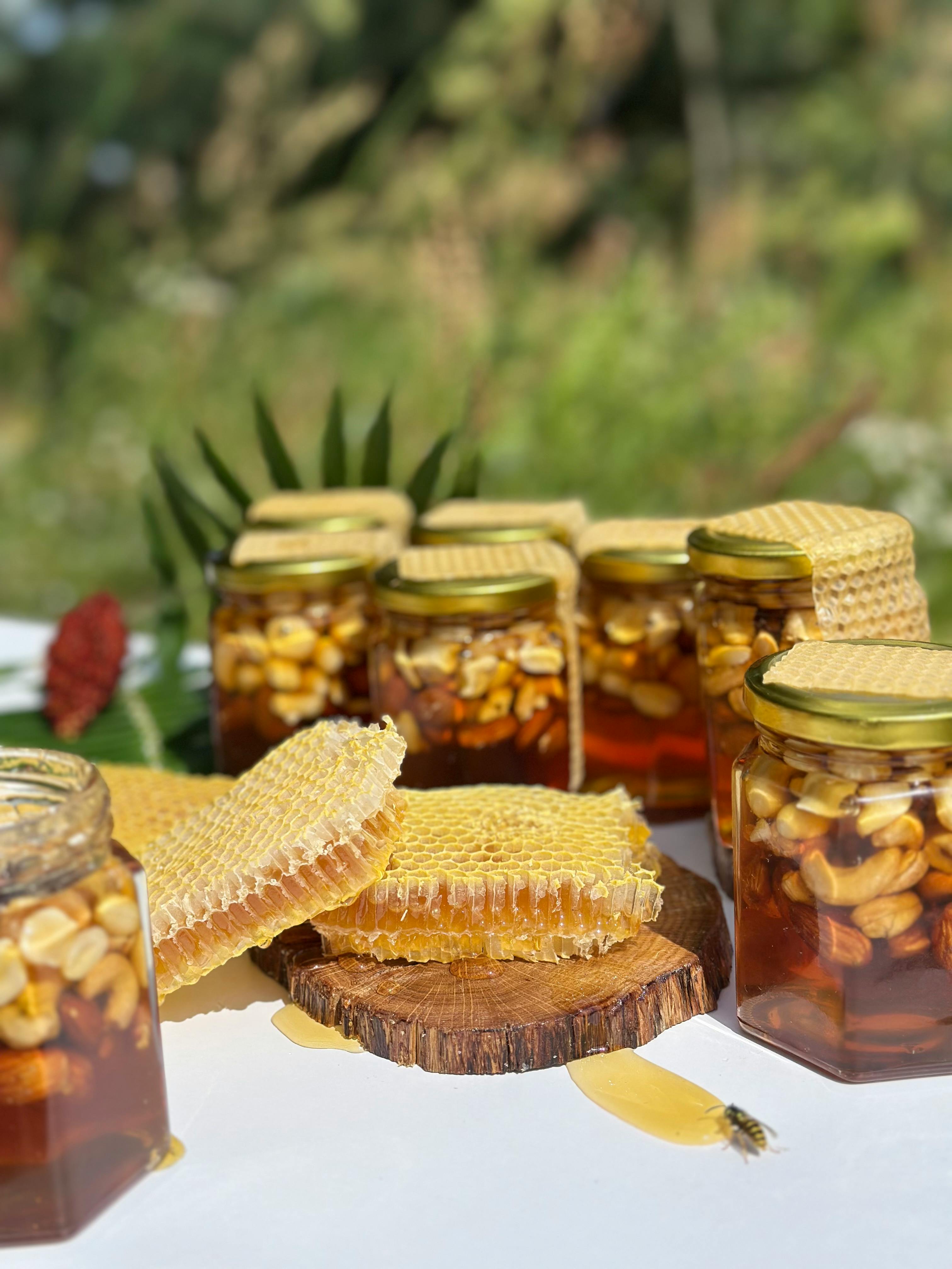 Glass jar of raw Ahaarmadhu organic honey surrounded by wildflowers and honeycomb